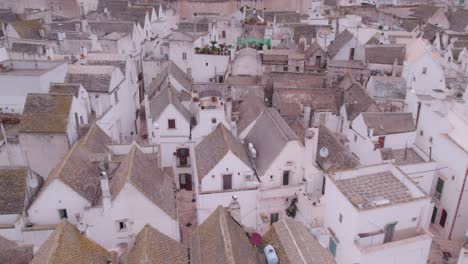 White-building-facades-in-historic-town-Locorotondo-with-large-church,-aerial