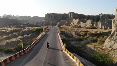 motorcyclist riding into distance on makran coastal highway road beside dramatic rock formations in hingol national park