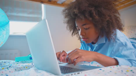 boy in bedroom lying on bed using with laptop with illuminated globe