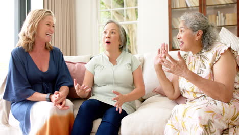 three senior women share a joyful moment on a couch at home