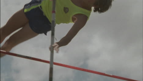 a young man does a pole vault lands on a mat and stands up smiling