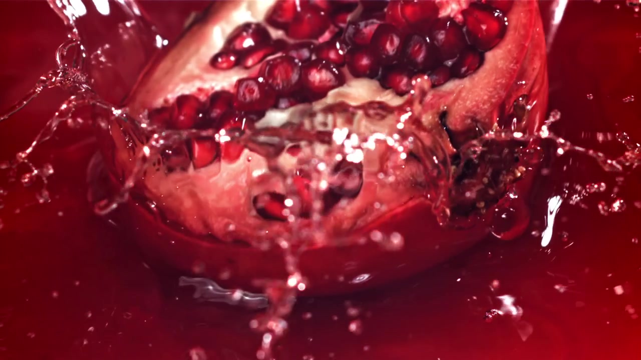 Slowmotion af et halvt granatæble der falder ned i rød saft