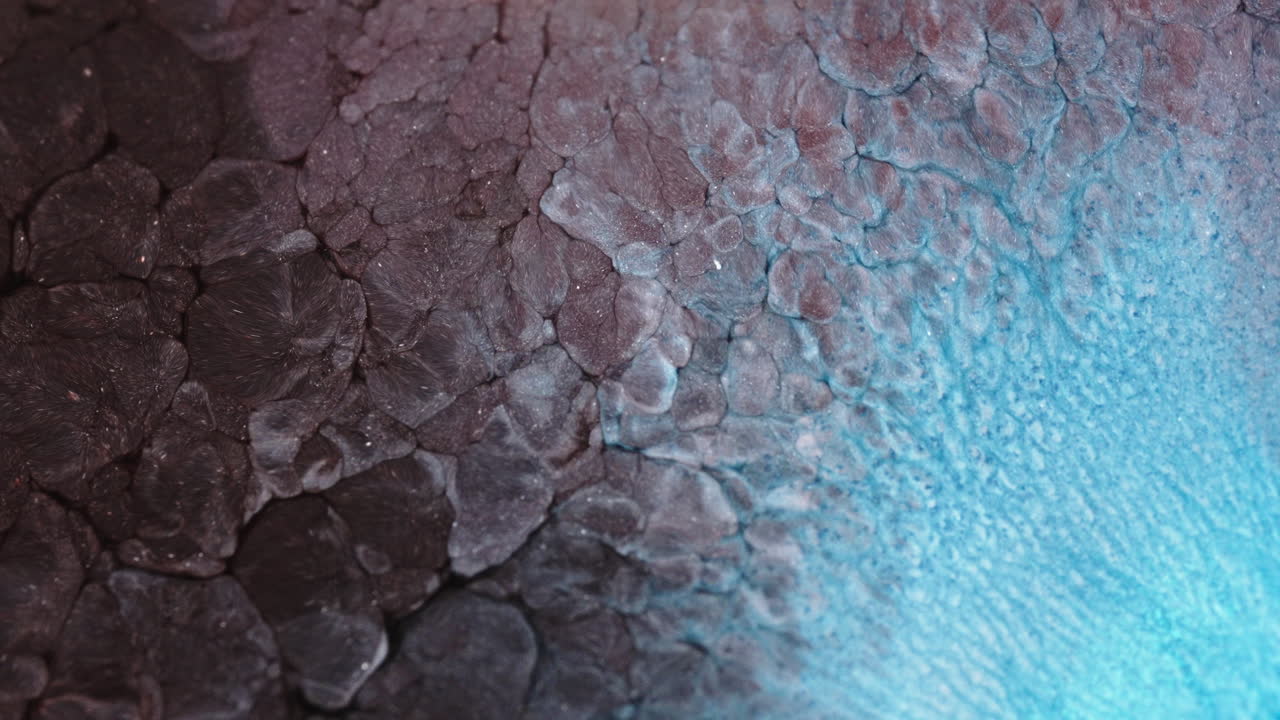 Colorful liquid spreads across a surface, creating abstract textures and patterns, macro view