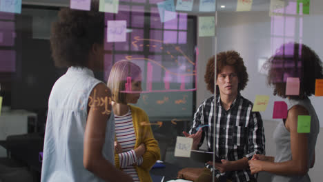 Diverse-work-colleagues-writing-and-drawing-on-glass-wall-having-a-discussion