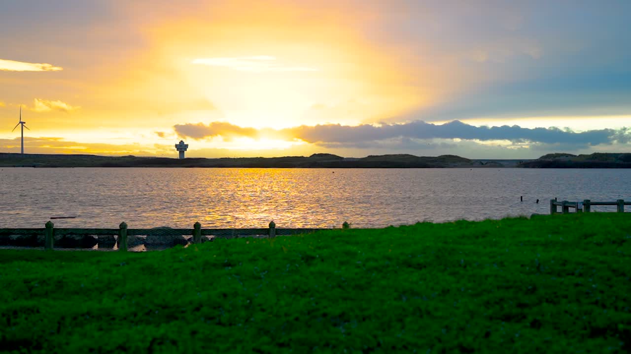차분한 물 표면과 멀리 있는 풍력 터빈을 가진 호수 위의 아름다운 일몰의 시간 경과