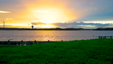 time lapse of a beautiful sunset over a lake with a calm water surface and a wind turbine in the distance