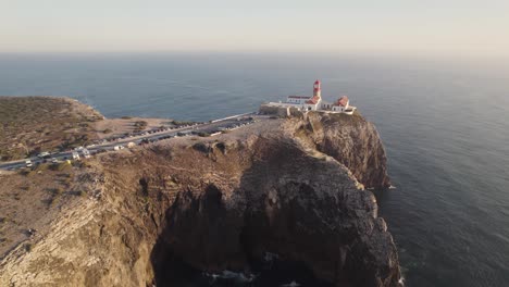 aerial of red and white striped lighthouse sitting on the edge of the cliffs in sagres, portugal