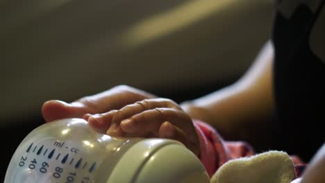 closeup of asian baby girl holding milk bottle while feeding