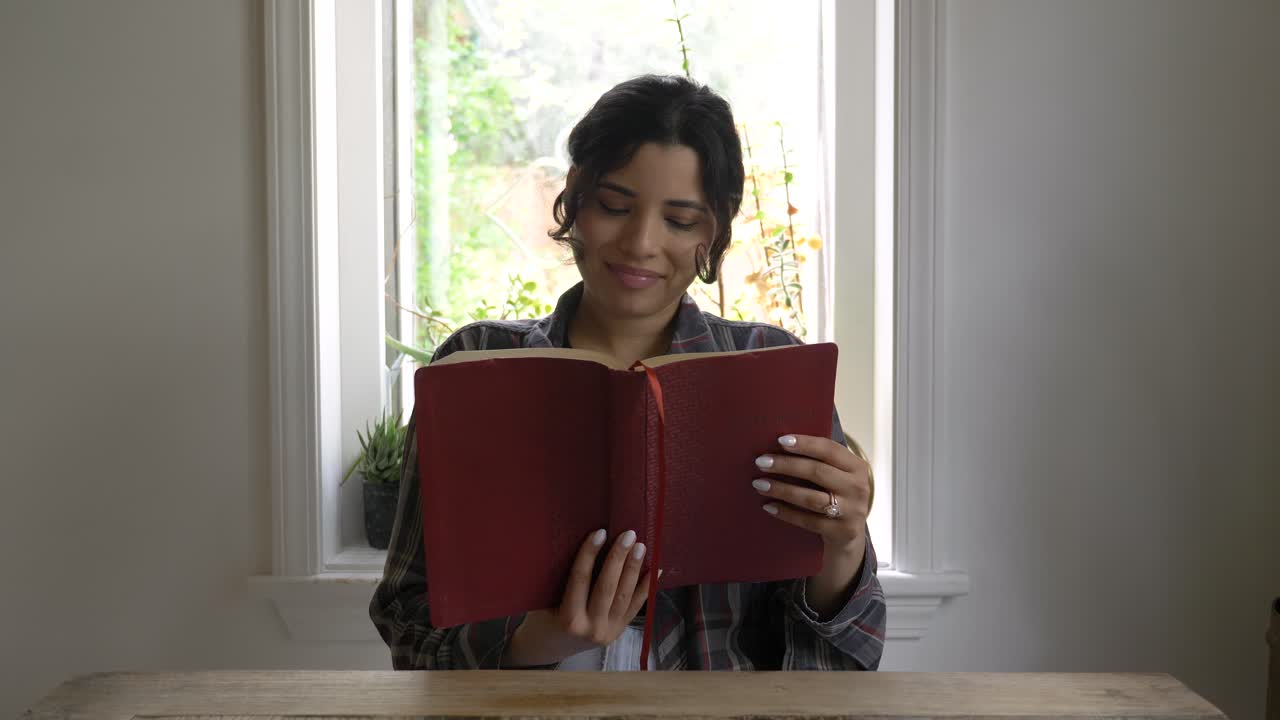 una feliz niña puertorriqueña leyendo la biblia en casa iluminada por la ventana