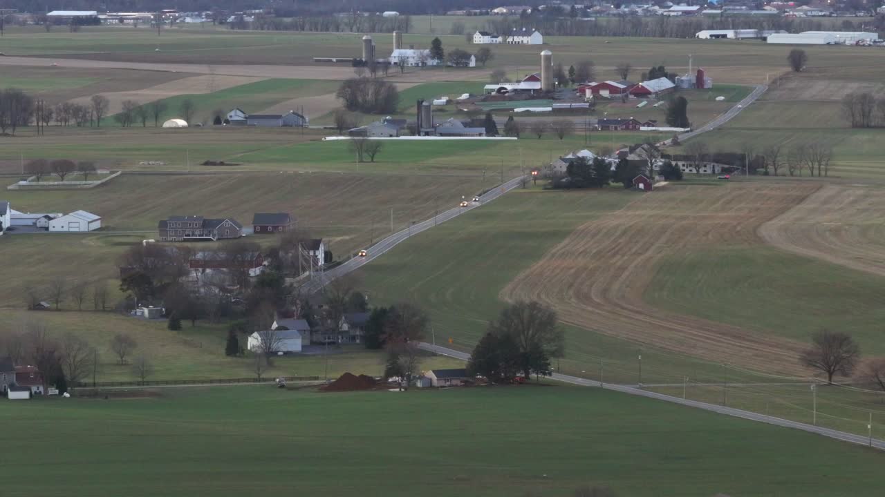 Driving cars on intersection during cloudy day in America. Farmers houses and silo storage in rural area of USA. Aerial wide shot. Barn and stables in countryside of PA, America.