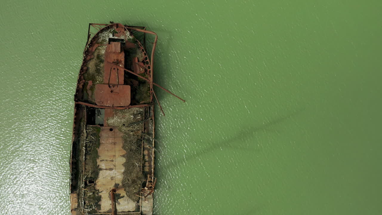 Rusty red shipwreck stuck in shallow green water
