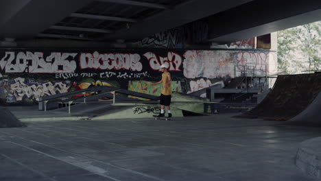 Young-skater-riding-on-skate-board-at-skate-park-with-graffiti-wall-background.