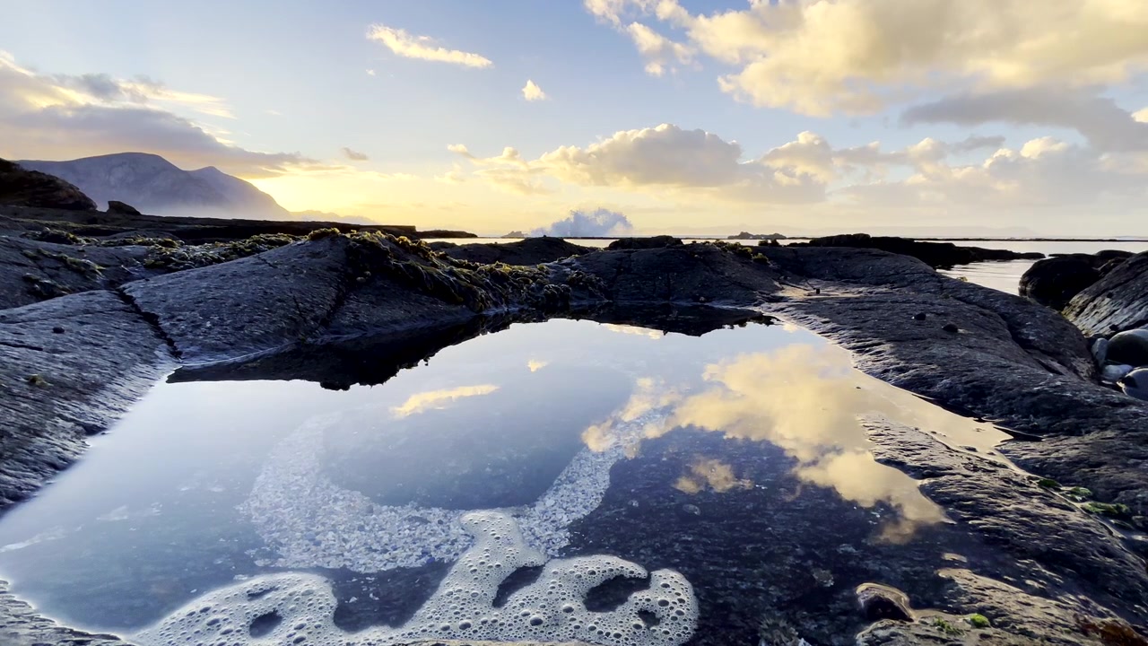 Betagende kystsolopgang med levende skyer reflekteret i en klippepøl ved havet, lav