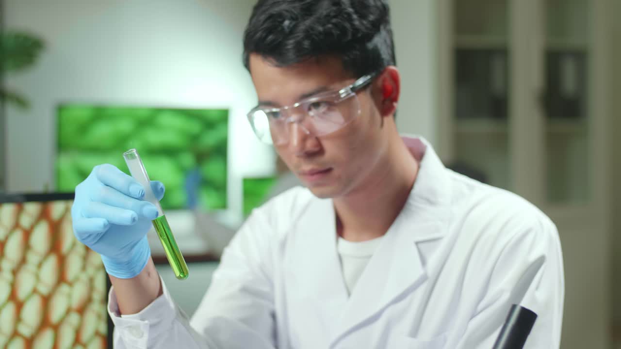 Asian Researcher Looking At Test Tube With Green Dna Of Sapling Analyzing Genetic Mutation Modified For Microbiology Experiment. Scientist Working In Agriculture Laboratory Developing Eco Environment