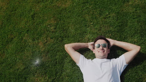 A-young-man-lies-on-the-grass-under-jets-of-water,-escapes-from-abnormal-heat