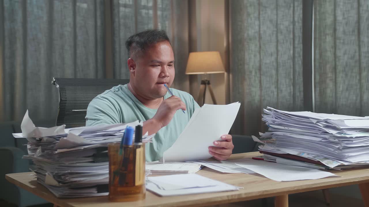 Fat Asian Man Thinking Then Taking Note While Working With Documents At The Office