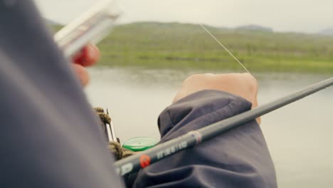 handheld close-up of young man fixing fly fishing rod at swedish lake