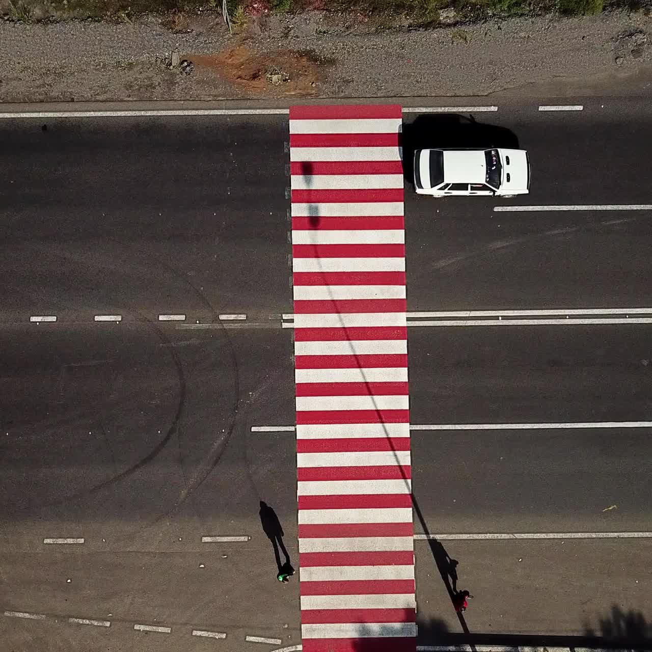 people are crossing the road on a pedestrian of red and white color on the background of the car. Aerial view