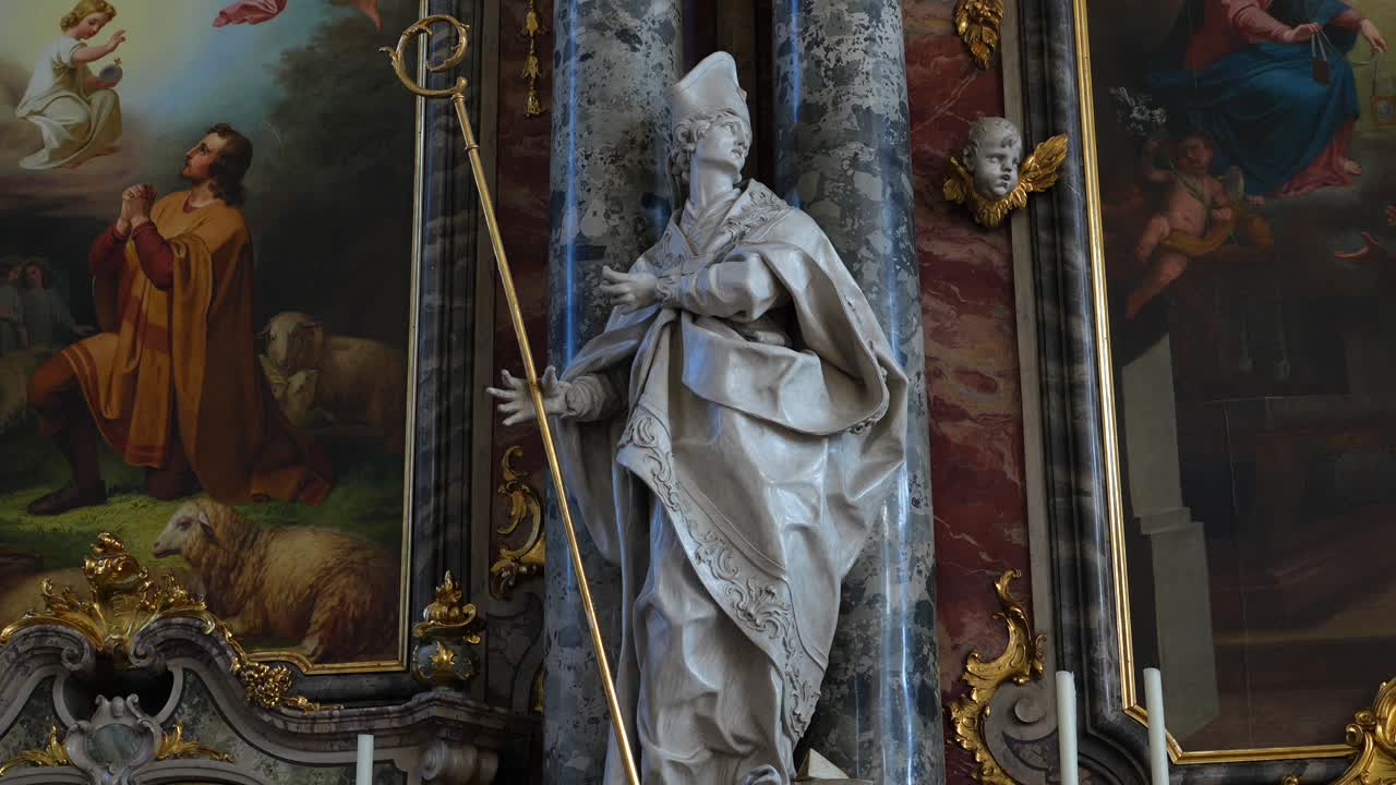 Detailní záběry sochy zobrazující svatého biskupa držícího hůl uvnitř katolického kostela.