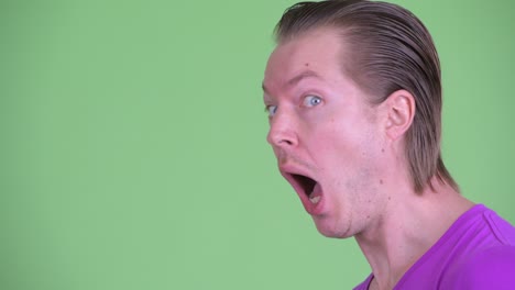 profile view zoom in shot of young man looking surprised and shocked against green background