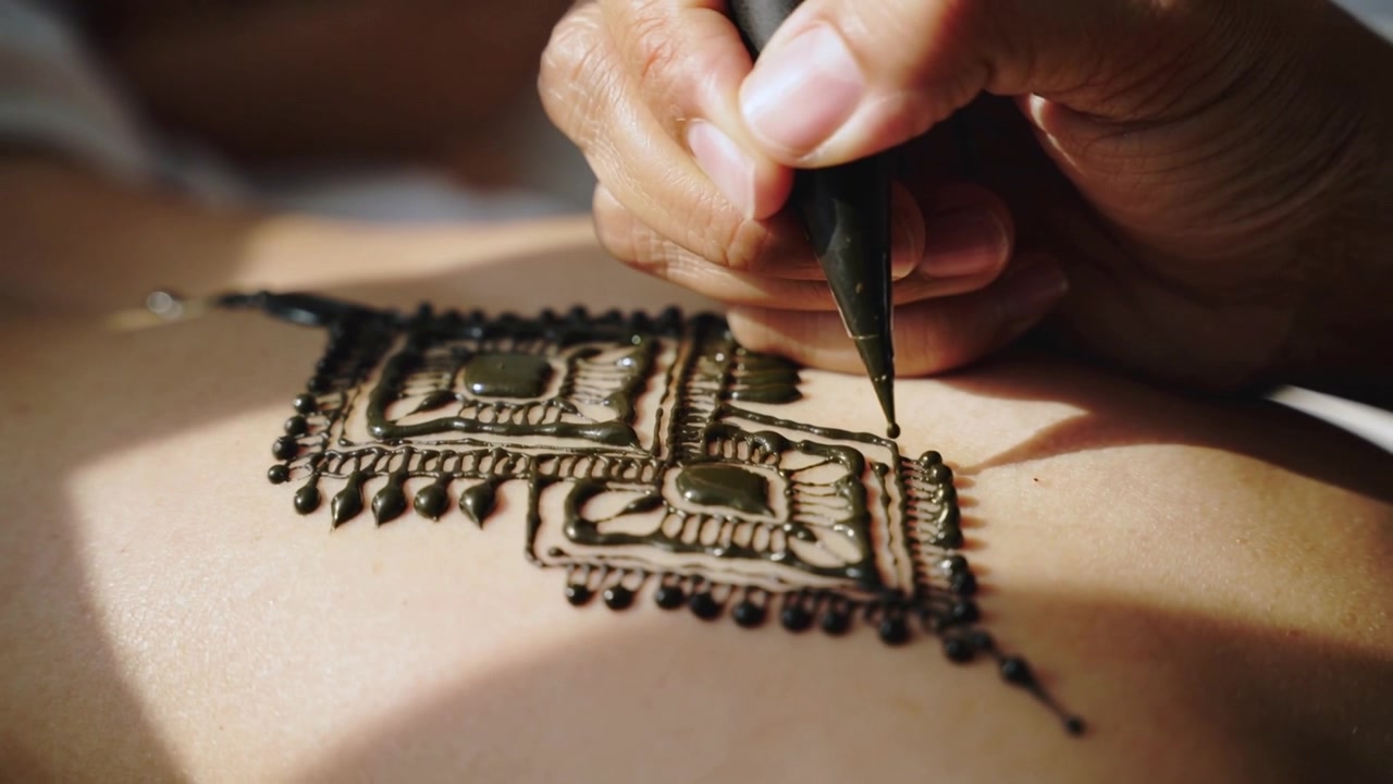 Mano di un artista di henné che disegna un motivo con pasta umida sulla pelle in studio, mentre il cono tocca.