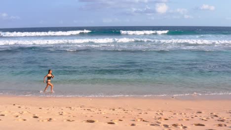 panning right shot of asian woman running along the shore of the beach in beautiful sunlight