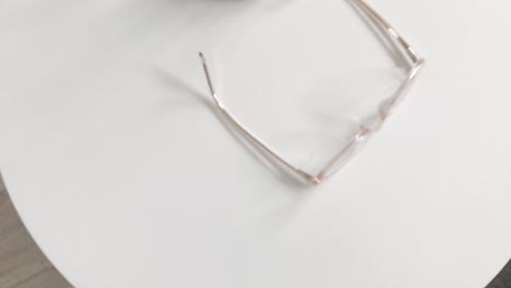 modern eyeglasses in light colour lie on a white table, bright glasses frame, slow motion footage