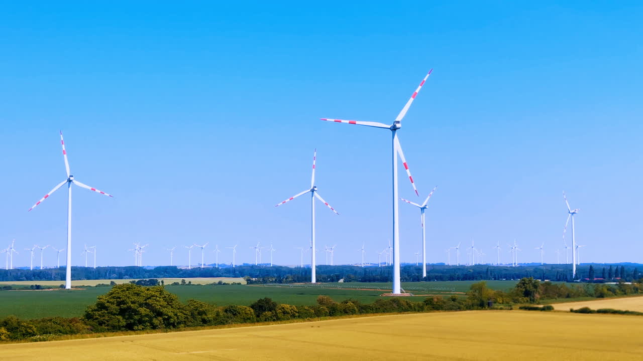 Daytime wind turbines in green. Wind turbines turn in the wind over a wide green field under a clear blue sky