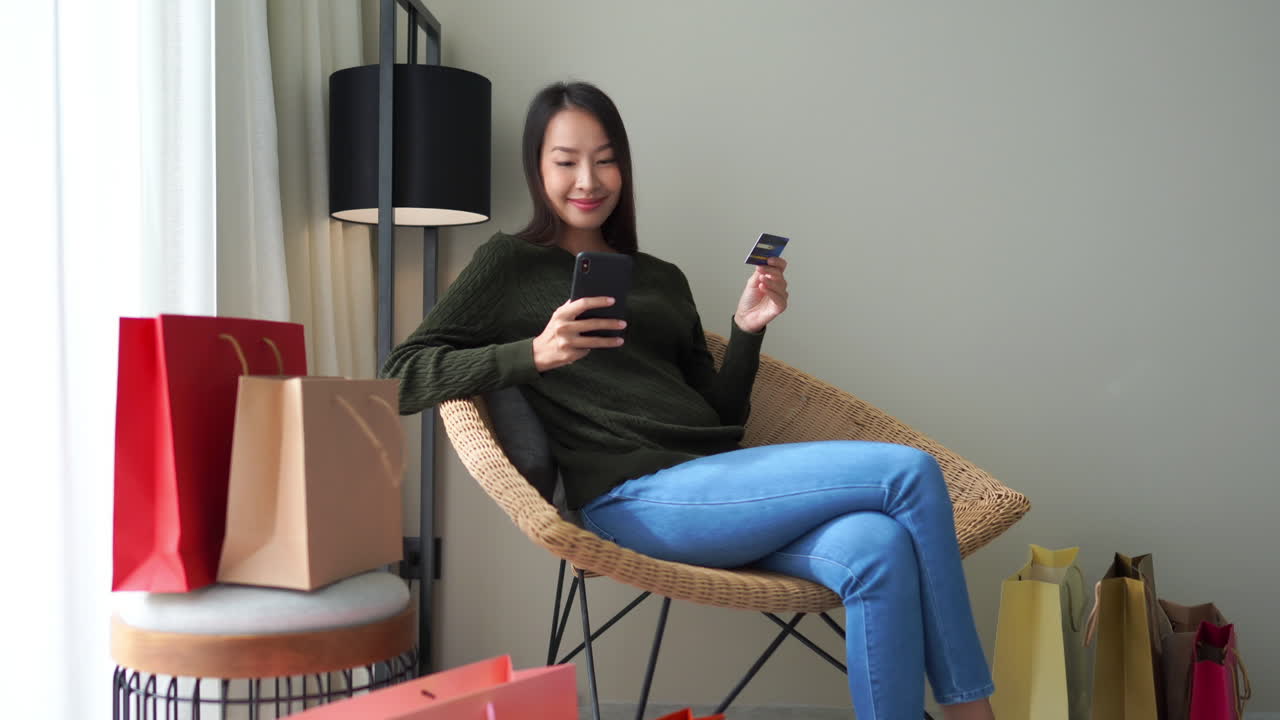 고리버들 의자에 앉아 신용카드와 휴대폰으로 다채로운 쇼핑백으로 둘러싸인 온라인 주문 품목을 들고 웃고 있는 소녀