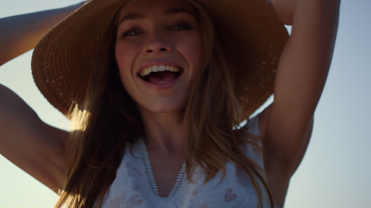 Donna felice che si gira con un cappello di paglia al tramonto. Giovane donna che ride nel parco.