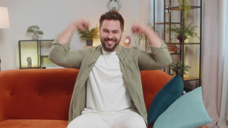 happy young man watching tv celebrating success winning lottery luck victory sitting on sofa