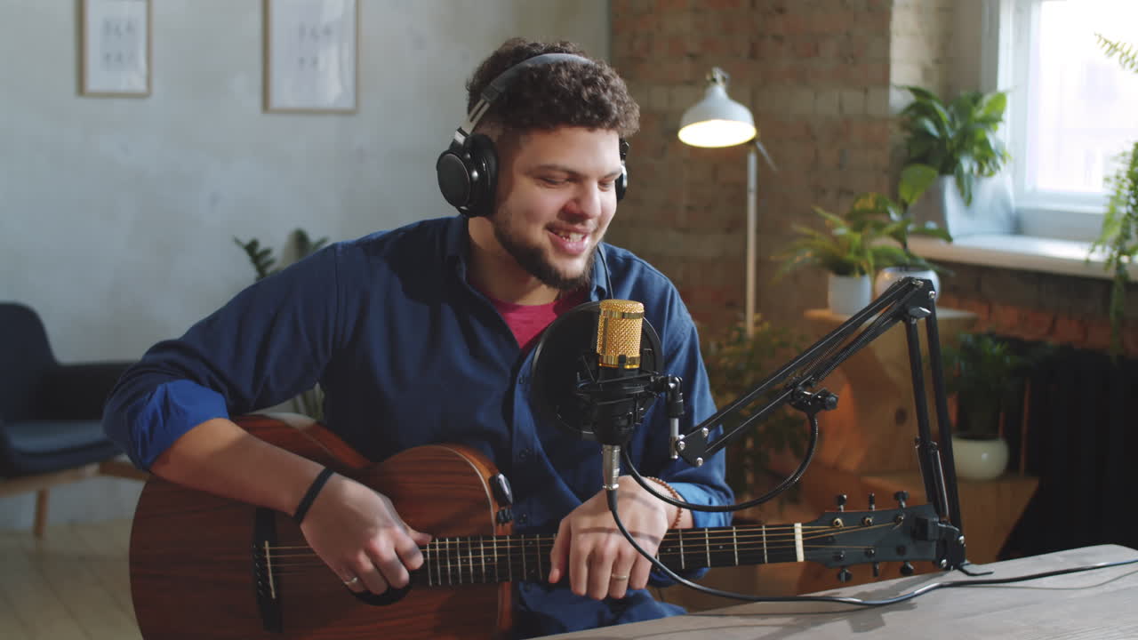 músico alegre con guitarra hablando ante la cámara en el estudio de grabación