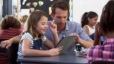 Teacher-and-young-schoolgirl-using-tablet-in-classroom