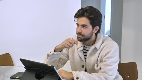 un joven apuesto trabaja en una tableta en la cocina sonríe a su esposa y envía un beso al aire