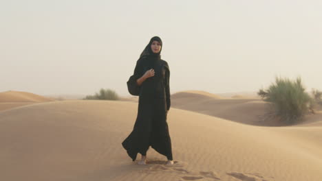 retrato de una hermosa mujer musulmana con hiyab caminando en un desierto ventoso y mirando la cámara 1