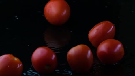 cherry tomatoes falling and rolling over in the water with a juicy reflection in the water in black background