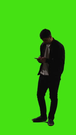 video vertical de larga duración de un joven que envía mensajes de texto en un teléfono móvil de pie contra la pantalla verde 3