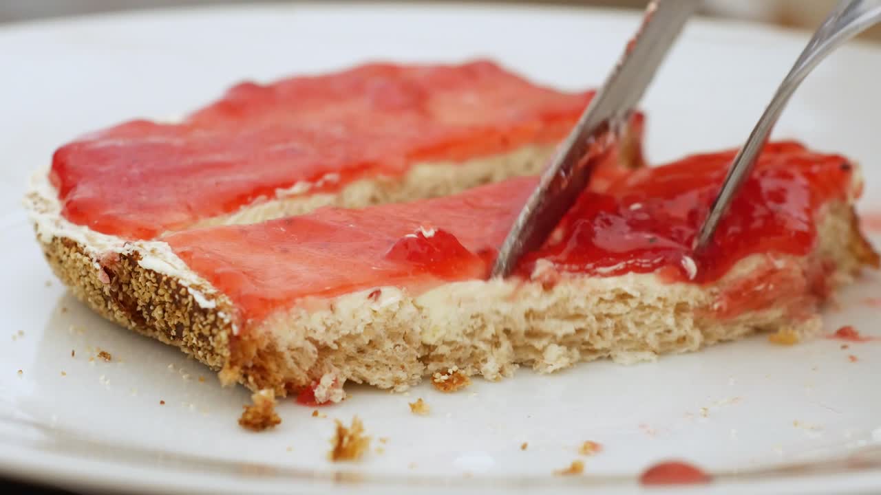Close up: fork and knife work together to cut a piece of strawberry jam bread