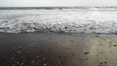 slow motion shot as waves washing out garbage from the ocean to the beach in bali