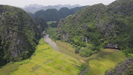 drone shot of river flows between mountain ranges with little boats going through small cave ninh binh viet nam
