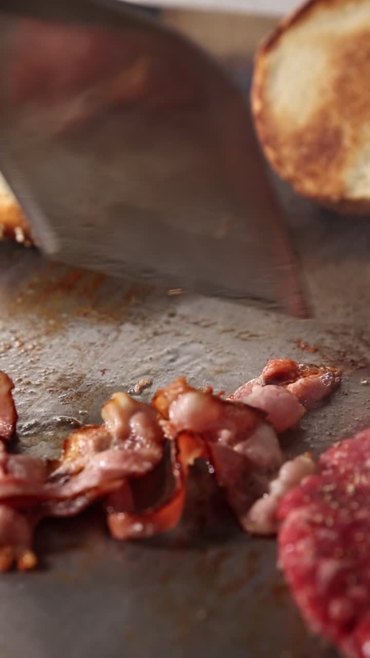 Pancetta sfrigolante e panini per hamburger che cuociono su una piastra calda