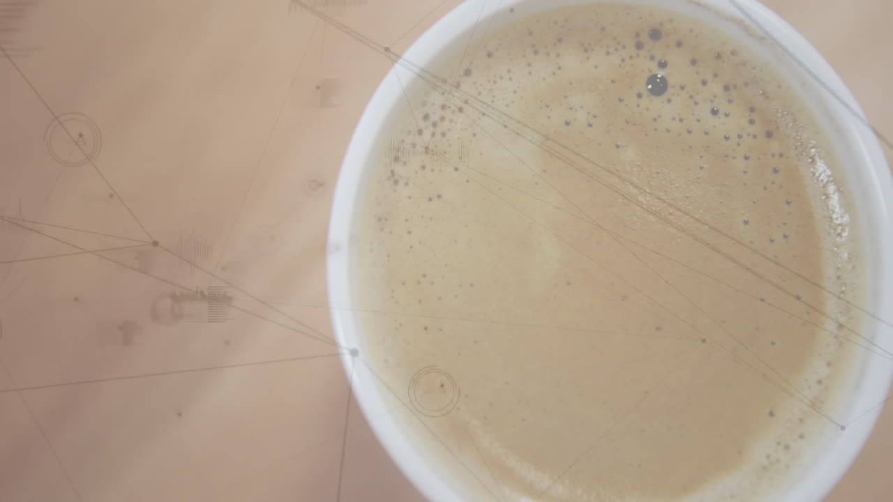 White ceramic cup being presented in closeup view, showing frothy coffee bubbles on wooden surface