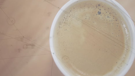 white ceramic cup being presented in closeup view, showing frothy coffee bubbles on wooden surface