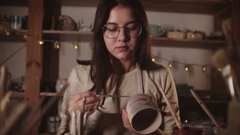 joven en el estudio de arte coloreando un producto de cerámica con un pincel y luego mira a la cámara
