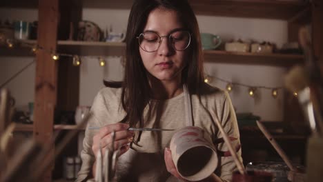 young woman in art studio coloring ceramic product with a brush then looks in the camera