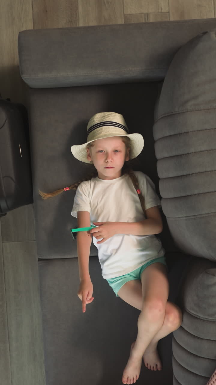 niña aburrida juega con gafas de sol acostada en el sofá en la habitación esperando la salida. lindo niño pequeño hermano camina con juguete de avión vista superior