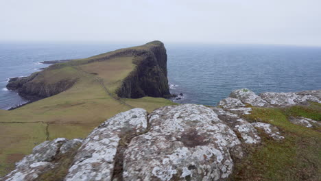 tracking shot of neist point lighthouse with rocky cliffs in foreground and atlantic ocean in the background on a windy and cloudy day in scotland, isle of skye