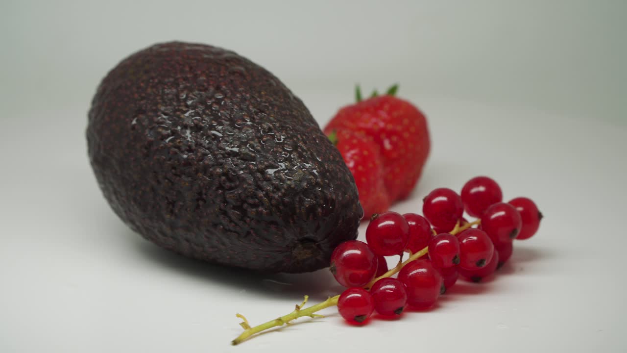 un conjunto saludable de frutas para el desayuno: aguacate maduro, grosellas rojas y fresas, primer plano