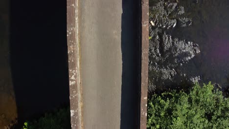 Male-with-purple-shirt-walks-over-narrow-stone-bridge-and-water-below