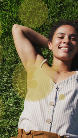 animación de manchas amarillas sobre una mujer biracial sonriente tendida en el parque